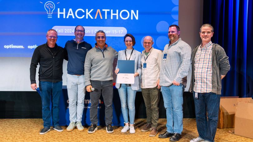 A group of Optimum employees pose together in front of a banner.